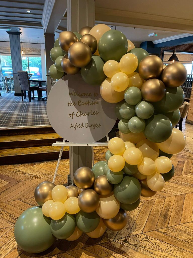 large balloon garland made of green, cream and gold balloons of different sizes to fame a welcome notice at a Christening