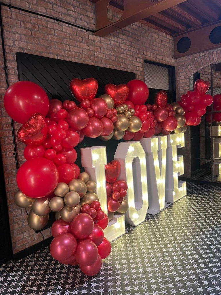 large created balloon garland on red and gold individual balloons sat around light up letters reading the word love.