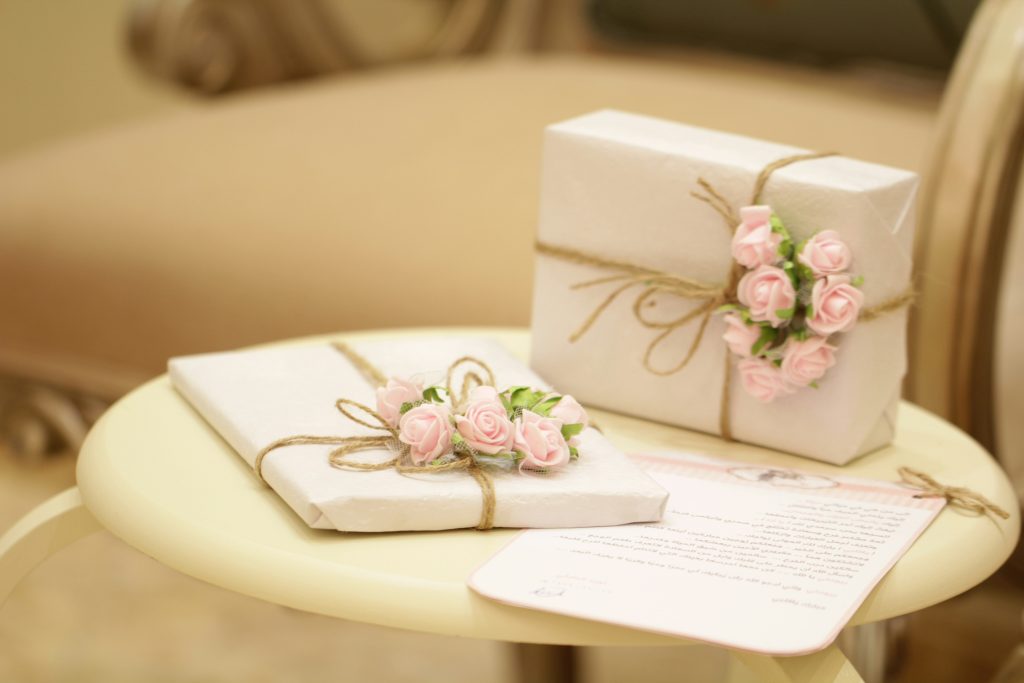 Wedding gifts wrapped in white paper with paper pink roses and tied in string on a table.