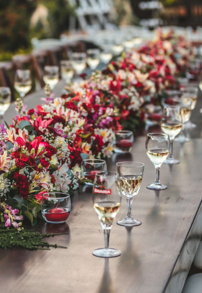 Wedding reception long table dressed with glasses and bright coloured flowers down the centre